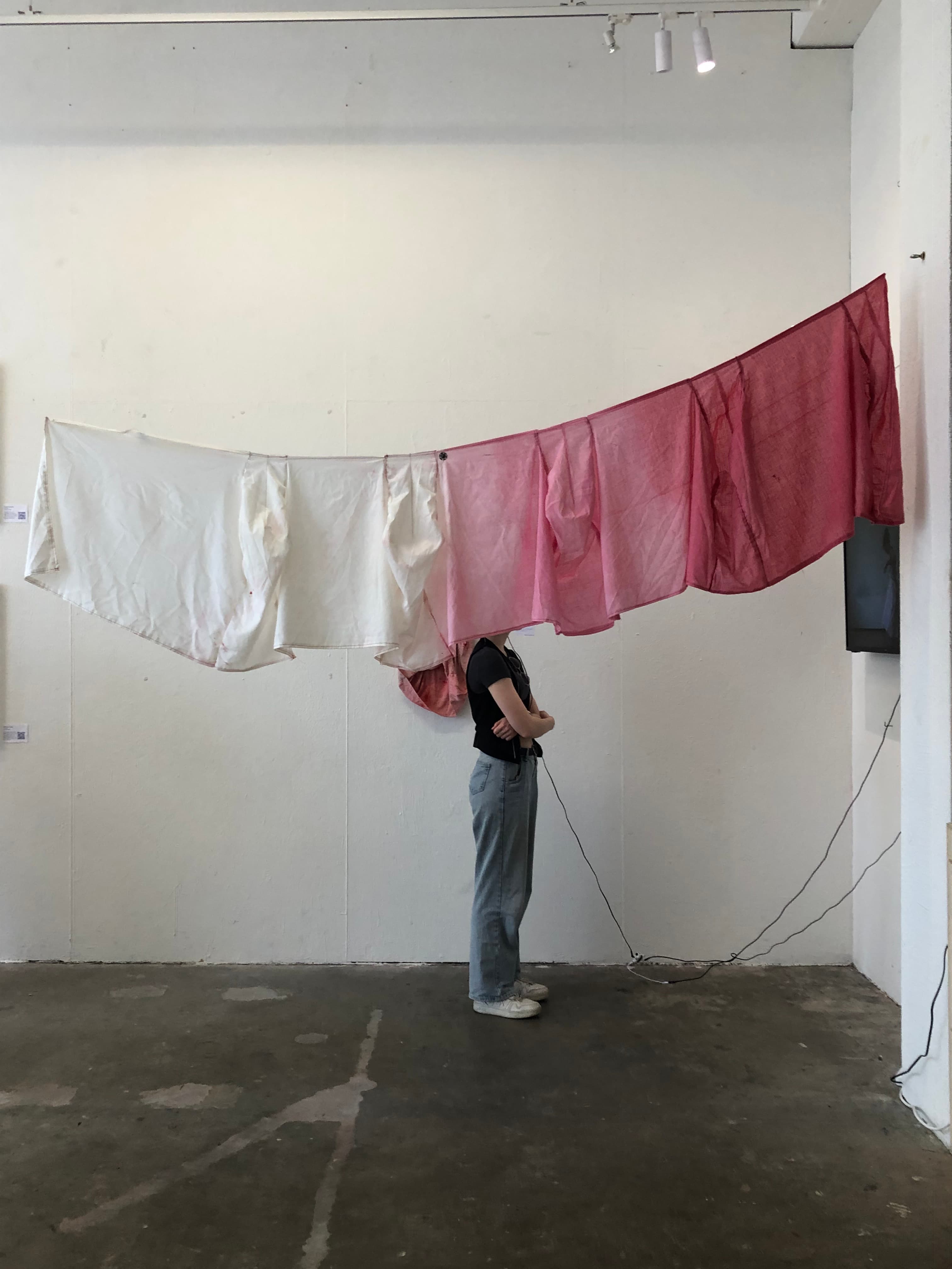 image of the textile work hanging, with someone standing behind it, their face covered