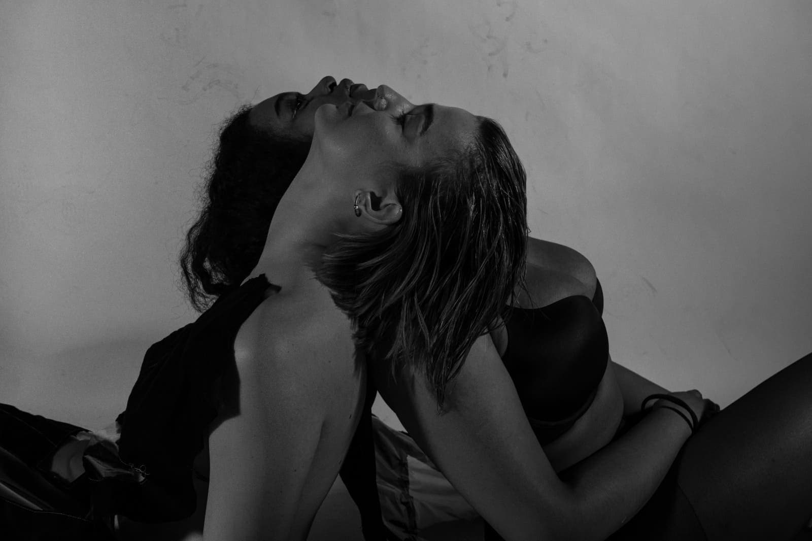 black and white image of woman laying on each other opposite shoulder back to back