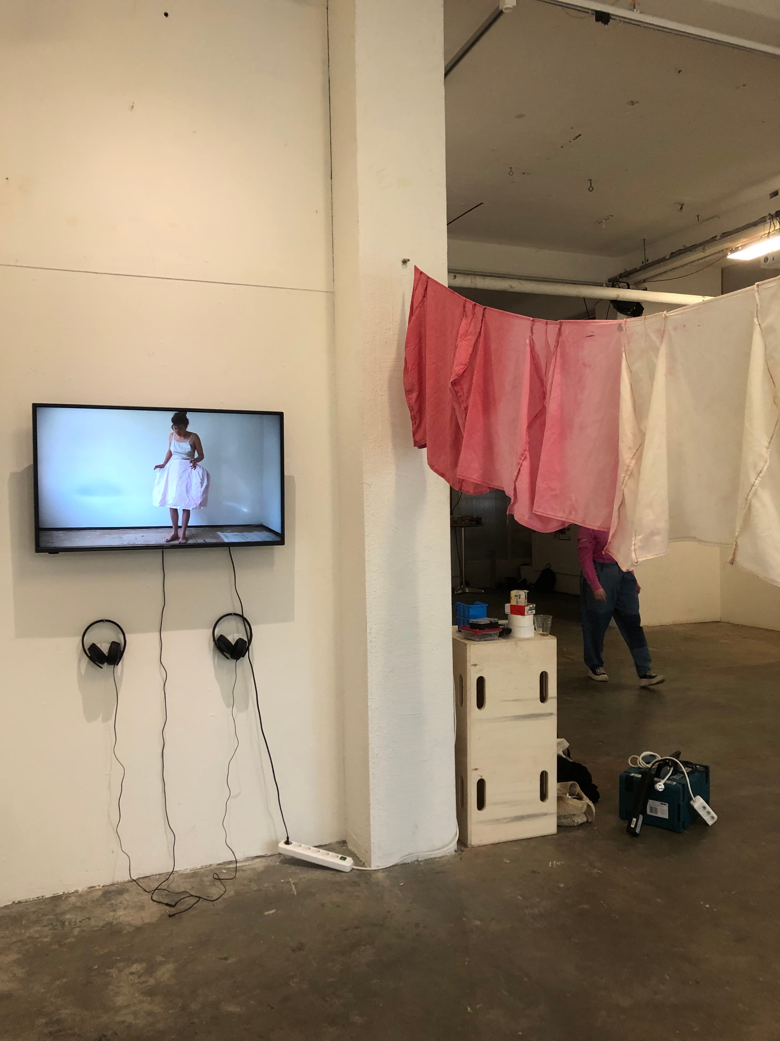 image of exhibition set up with tv on the wall playing a video and a piece of textile strung horizontally